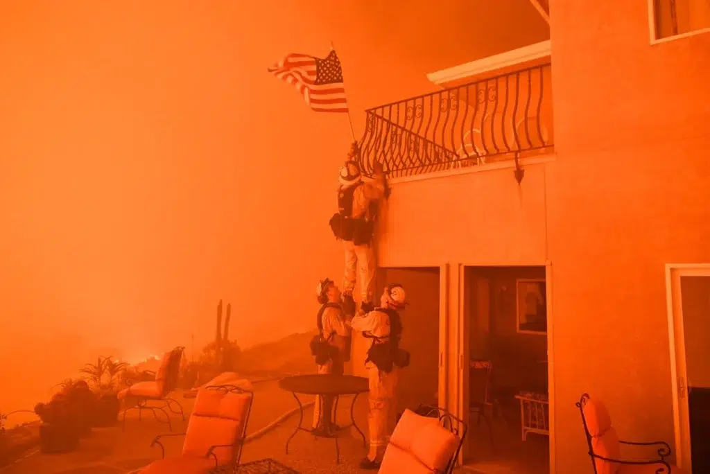 A firefighter rescues an American flag as smoke turns the sky orange at the Wall Fire near Oroville, California, in 2017. (Josh Edelson / AFP)