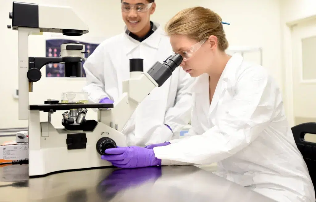 Scientist looking into a microscope while a colleague observes in a research laboratory, life sciences photography in the San Francisco Bay Area
