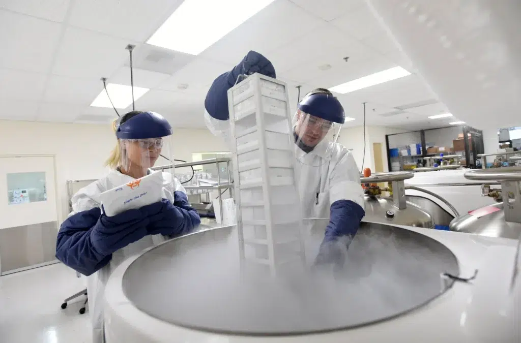 Two lab technicians in cleanroom PPE retrieving samples from a cryogenic storage tank, healthcare and life sciences photography by Josh Edelson