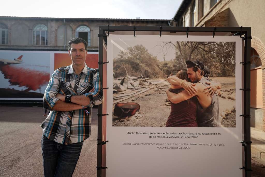 Josh Edelson standing beside his wildfire photograph exhibited at Visa pour l'Image, the international photojournalism festival in Perpignan, France