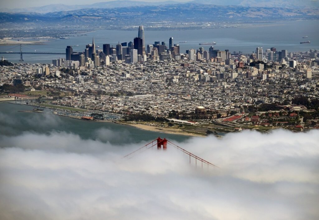 Aerial view of the San Francisco skyline with the Golden Gate Bridge in the foreground and marine fog rolling in across the bay — aerial photographer Josh Edelson