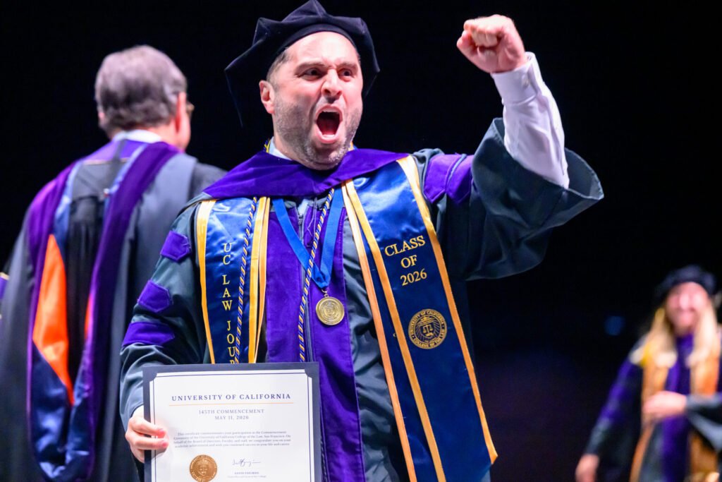 UC Law San Francisco Class of 2026 graduate celebrates with fist pump after receiving diploma at commencement — photo by Josh Edelson