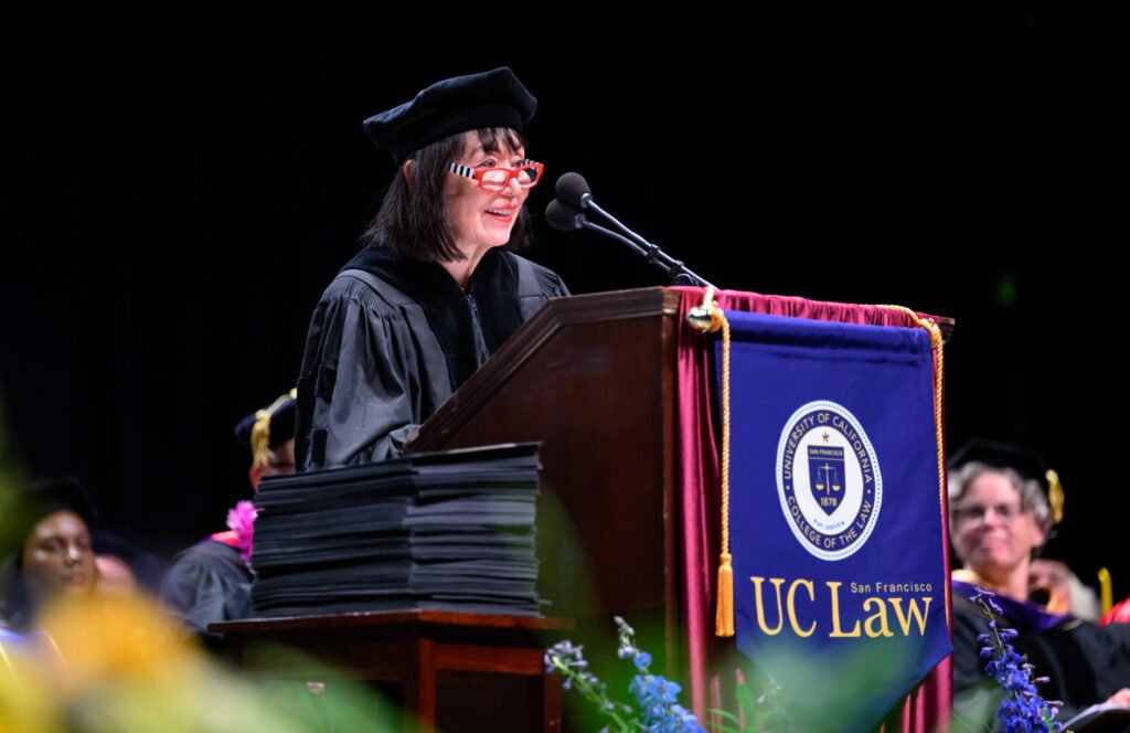 UC Law San Francisco graduate holds diploma at commencement branded backdrop — photo by Josh Edelson