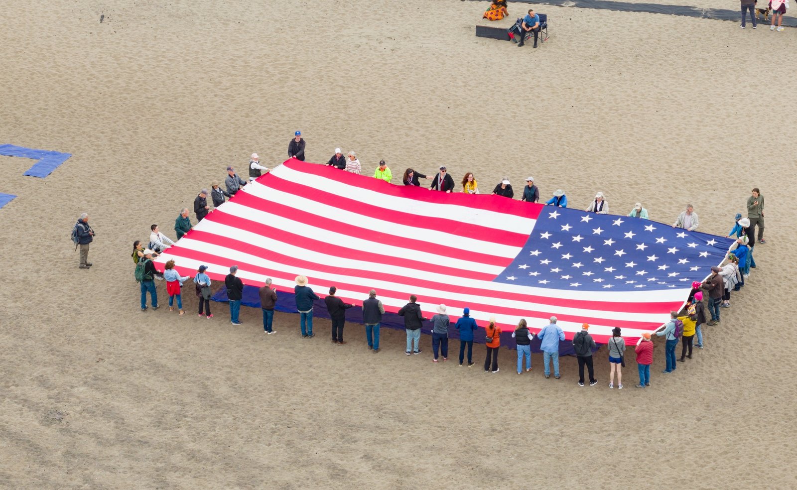 Aerial drone photo of demonstrators holding a giant American flag on the sand at Ocean Beach, San Francisco, during the Epstein files protest