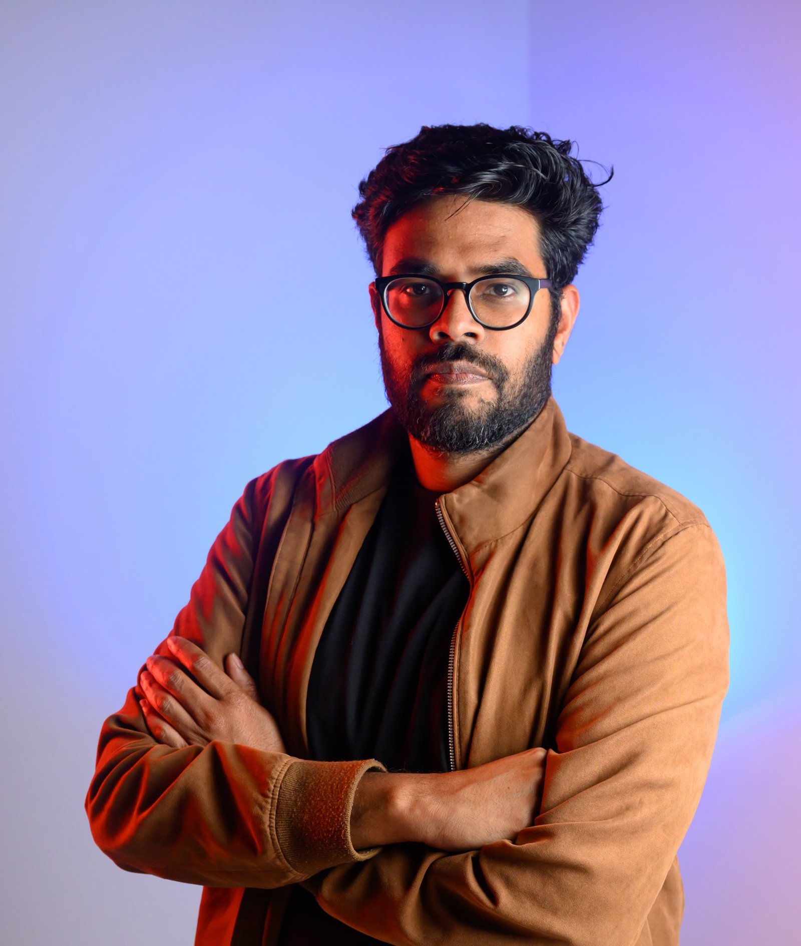 Studio-style portrait of Luma AI CEO Amit Jain lit with three gelled flashes, a red gel on the left, a key light through an umbrella on the right, and a blue gel behind him, shot in Palo Alto by Josh Edelson for the Los Angeles Times