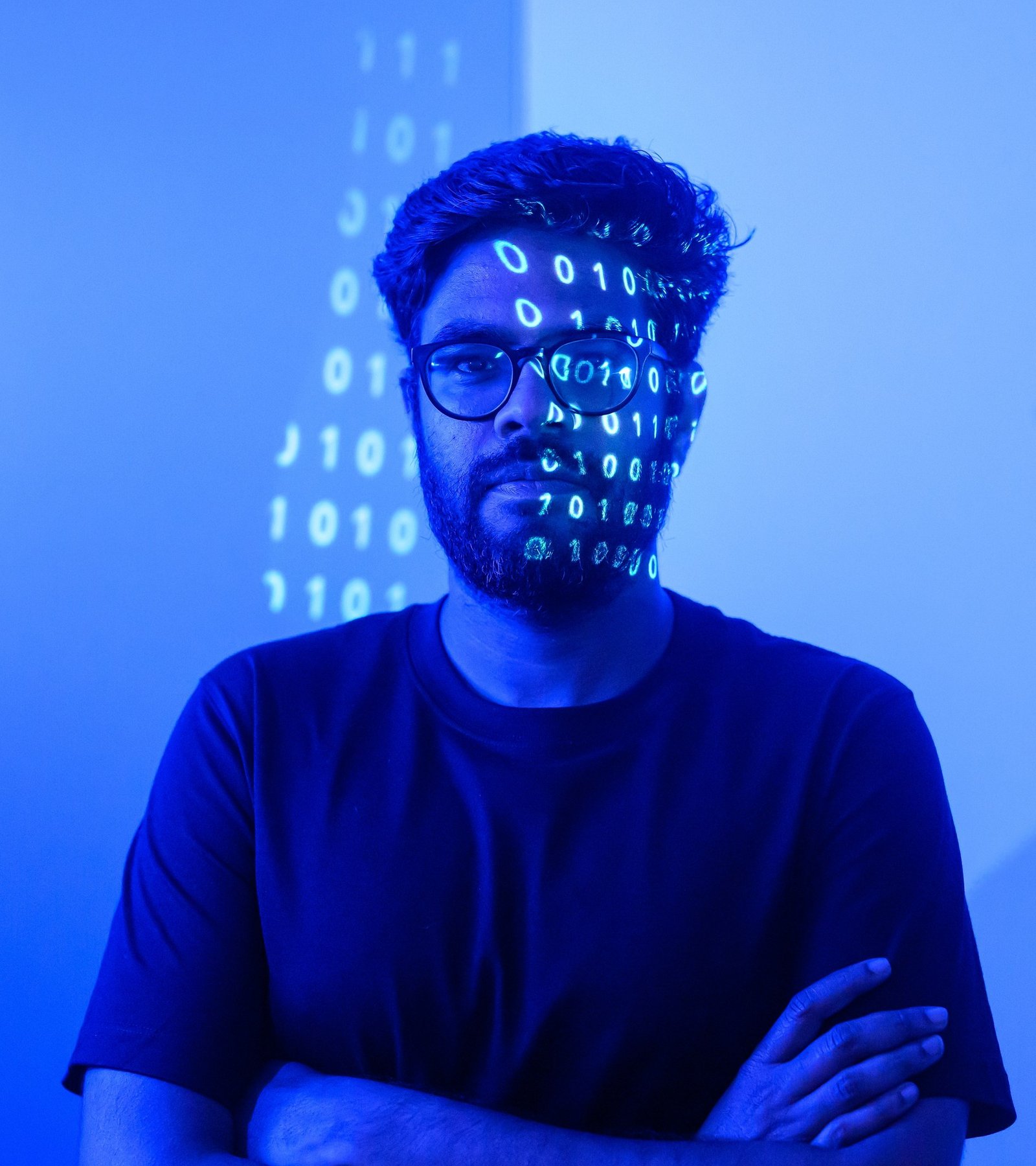 Portrait of Luma AI CEO Amit Jain with AI-generated code projected across his face, the blue-lit result shot in a blacked-out bathroom in Palo Alto, by Josh Edelson for the Los Angeles Times