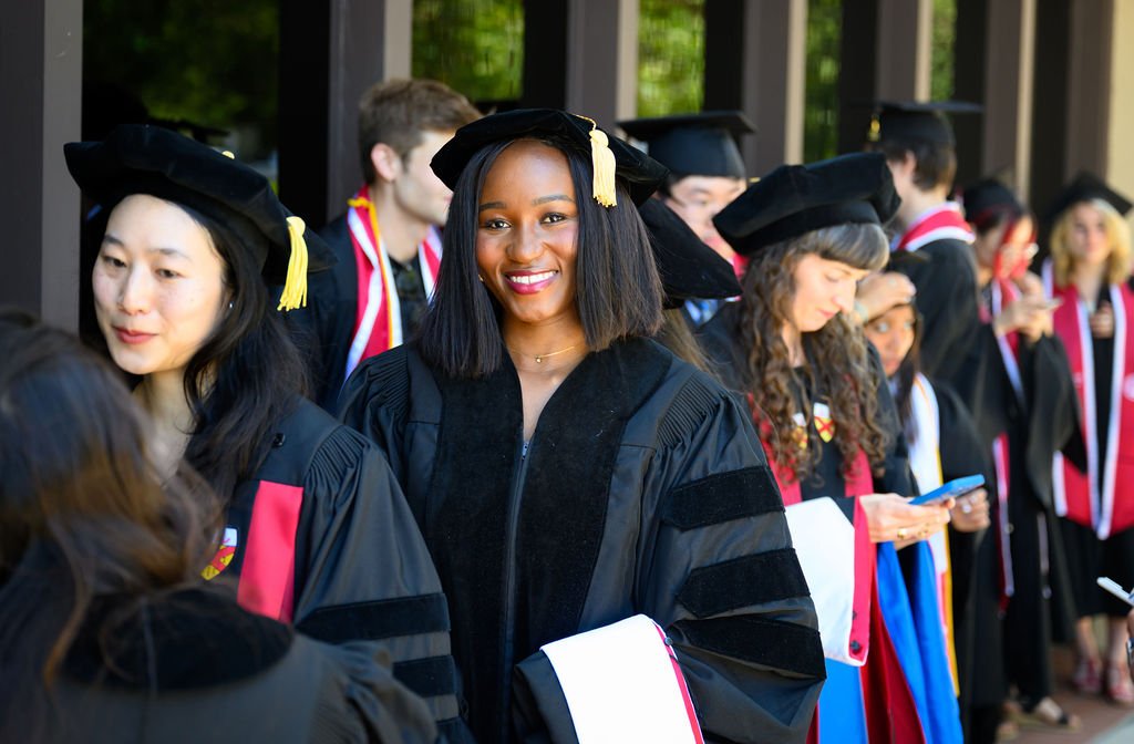 Doctoral graduates in cap and gown smiling in the procession line at the Stanford DLCL commencement