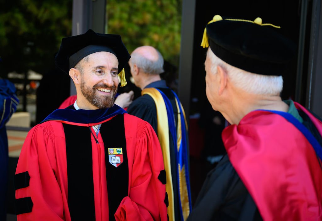 A doctoral graduate in red Stanford regalia talking and smiling with a faculty member before the DLCL commencement