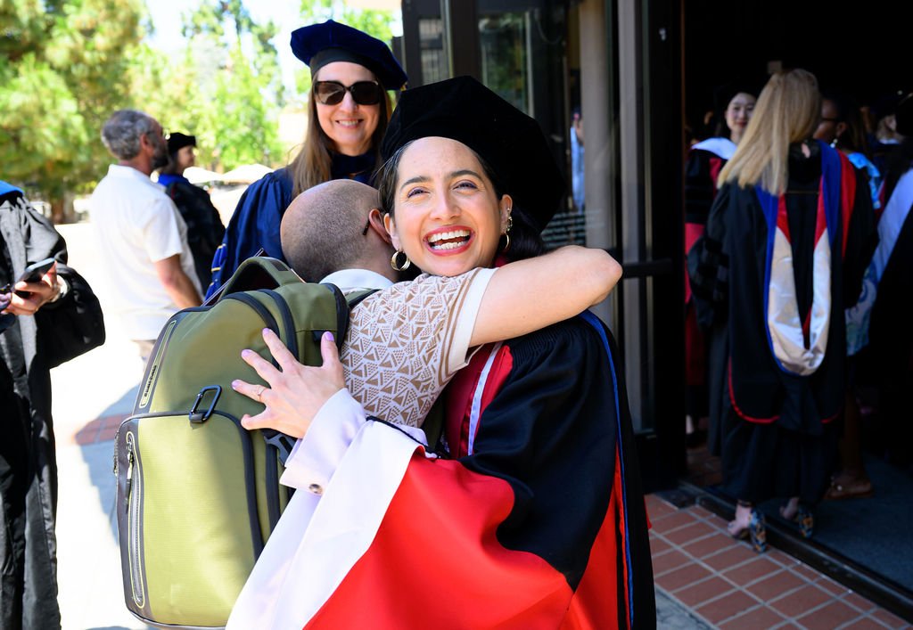 A doctoral graduate beams while hugging a loved one outside after the Stanford DLCL commencement