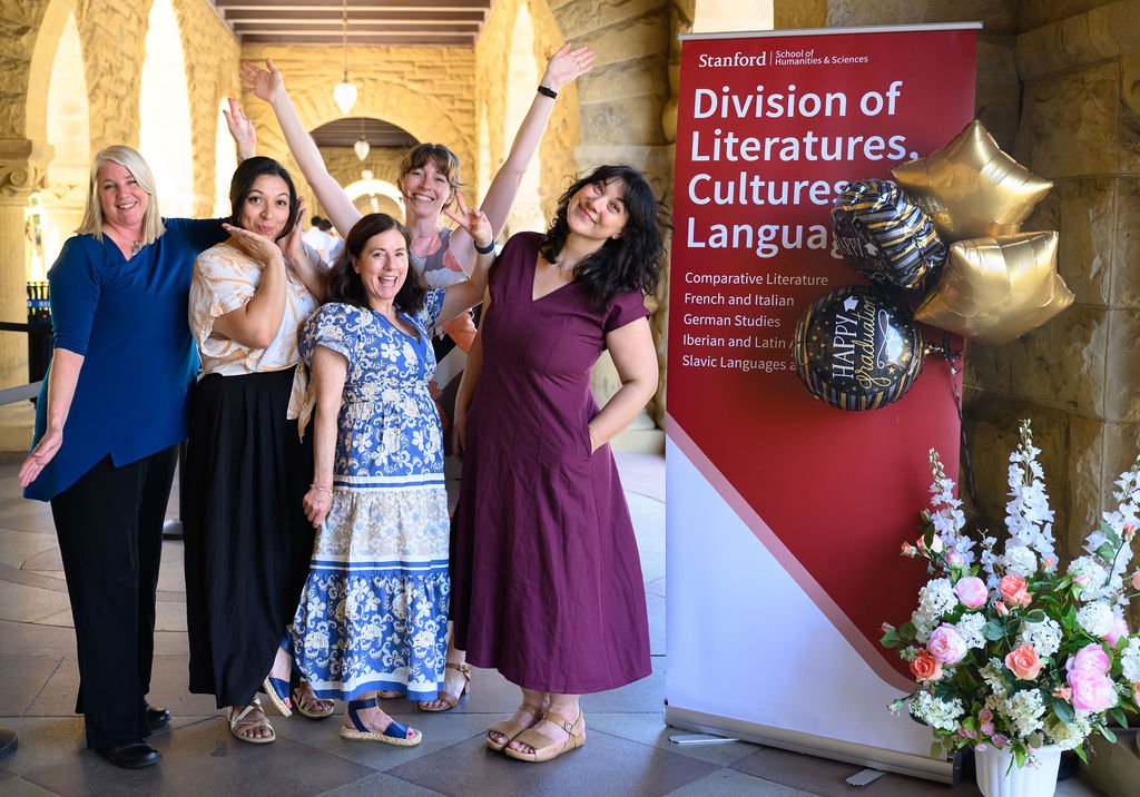 Graduates and faculty cheering beside the Division of Literatures, Cultures, and Languages banner under Stanford’s sandstone arches