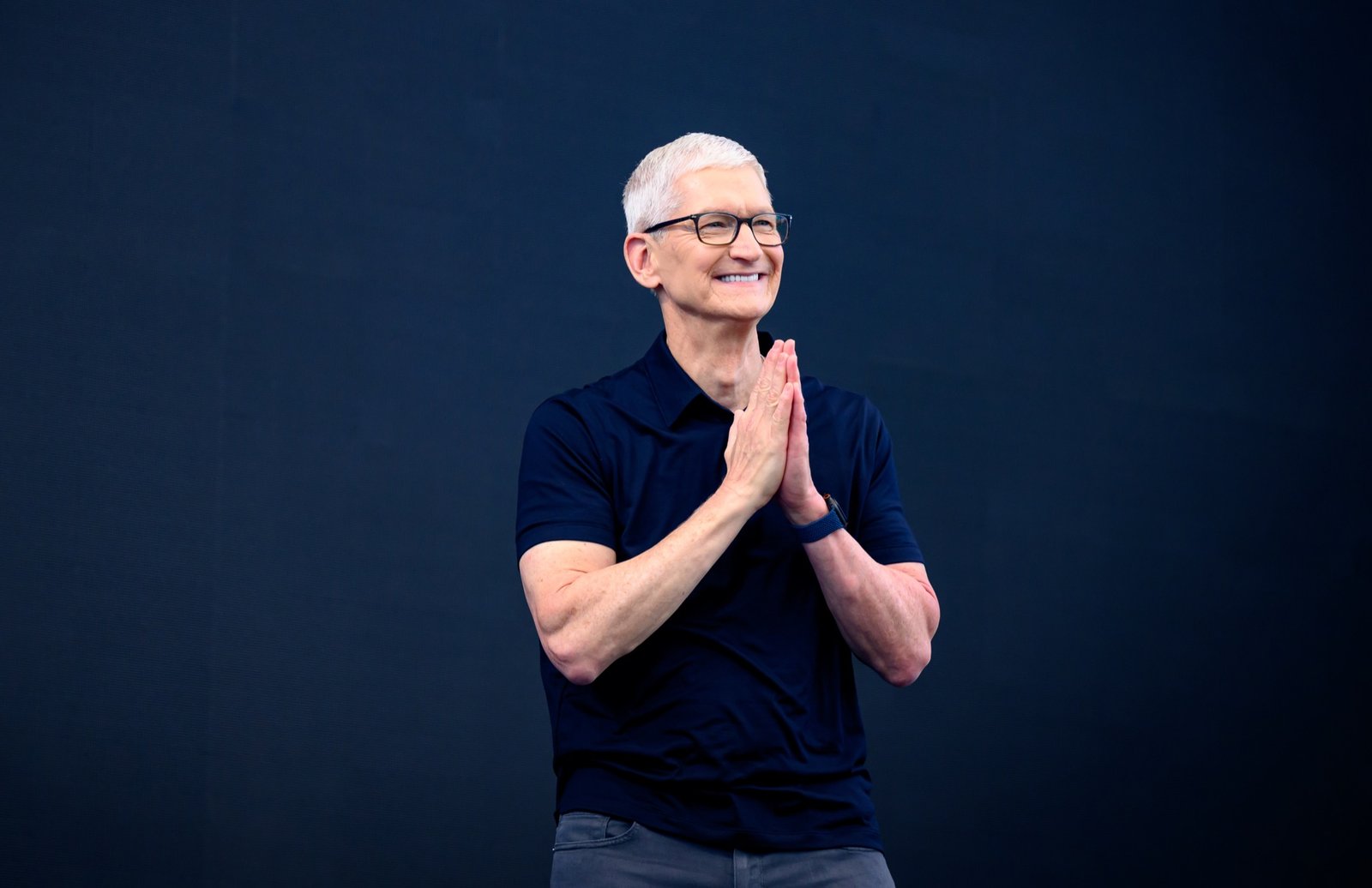 Apple CEO Tim Cook pressing his hands together in a grateful gesture, smiling, at the 2026 WWDC keynote