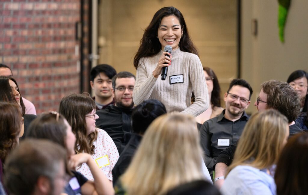 An attendee smiling while asking a question at a corporate event, event photography by Josh Edelson