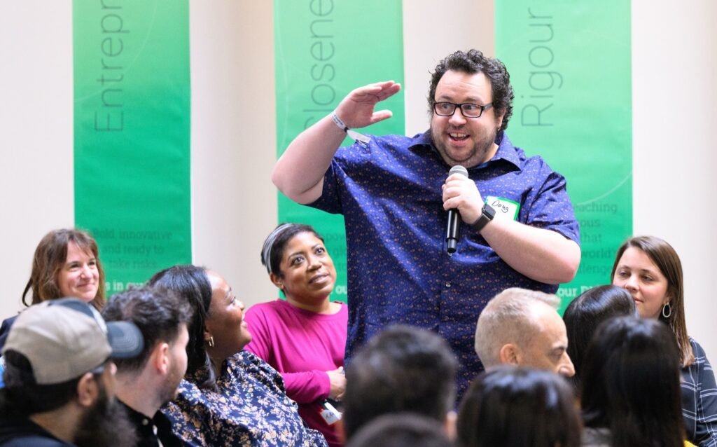 An attendee speaking at a corporate event in front of company values banners, by Josh Edelson