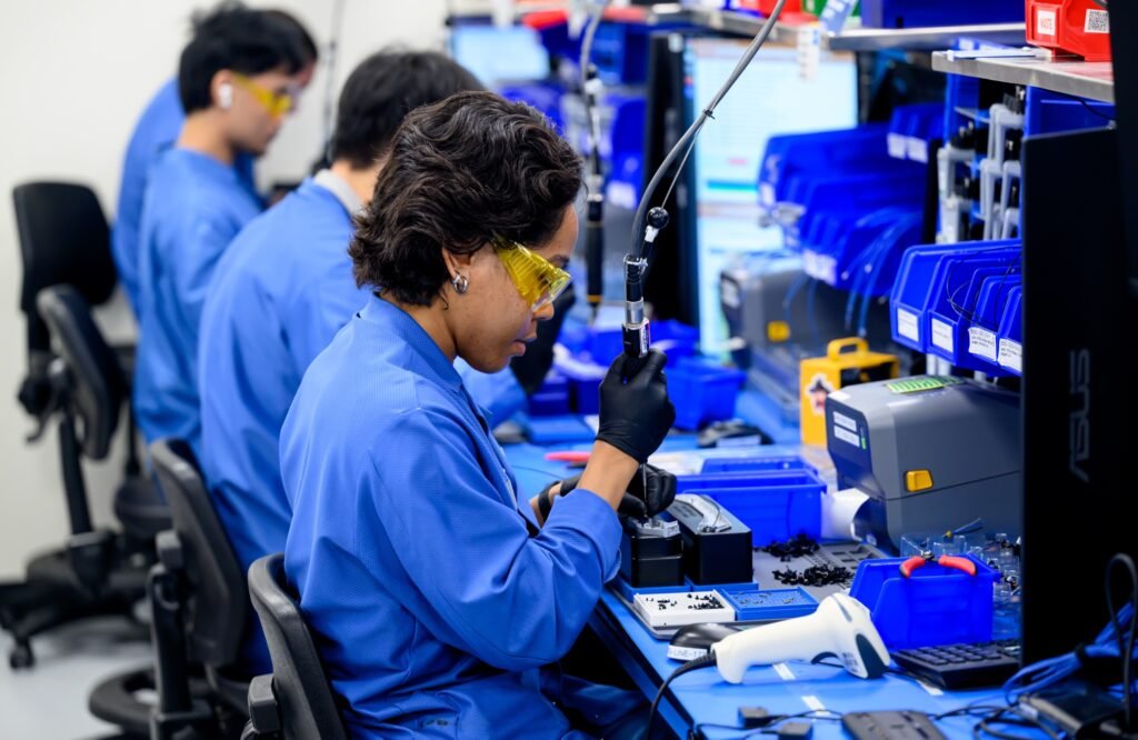 Engineer wearing safety glasses using a precision tool at an assembly workbench, corporate lifestyle photography in the San Francisco Bay Area