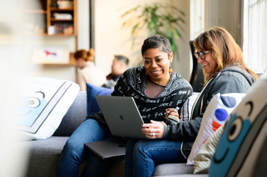 Two colleagues collaborating on a laptop in a bright office lounge, corporate office and lifestyle photography by Josh Edelson