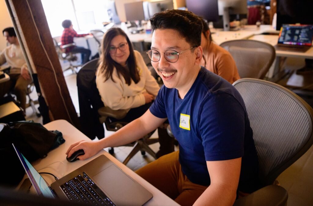 A team member smiling at a laptop in an open-plan San Francisco office, corporate office and lifestyle photography by Josh Edelson