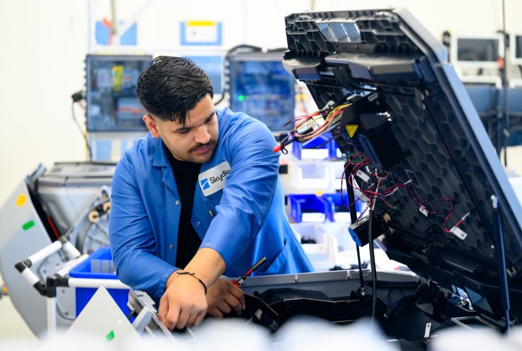 Technician in a blue lab coat working on electronics at a Bay Area technology manufacturing facility, corporate lifestyle photography by Josh Edelson