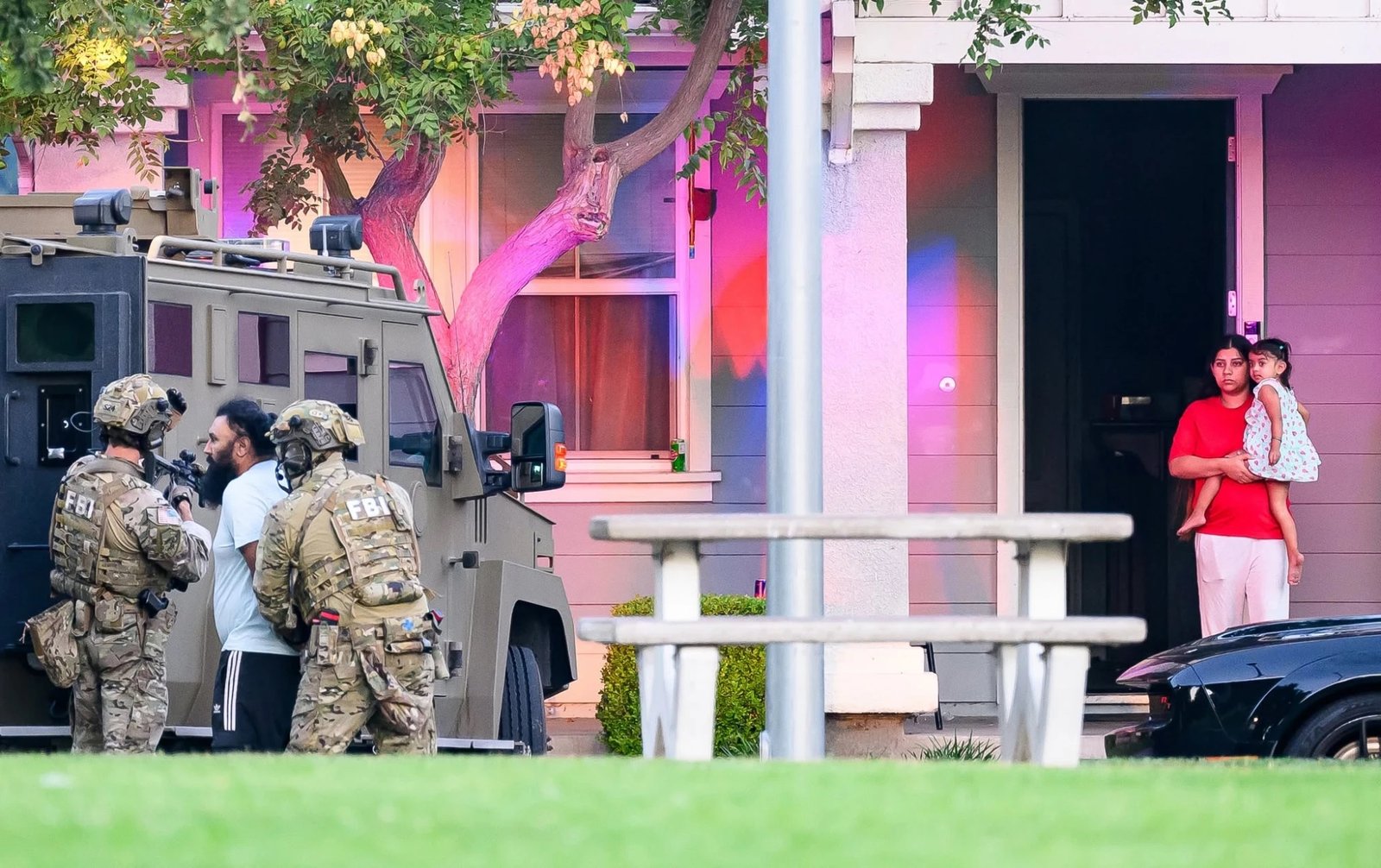 Agents lead a suspect toward the armored vehicle as his family watches from the doorway.