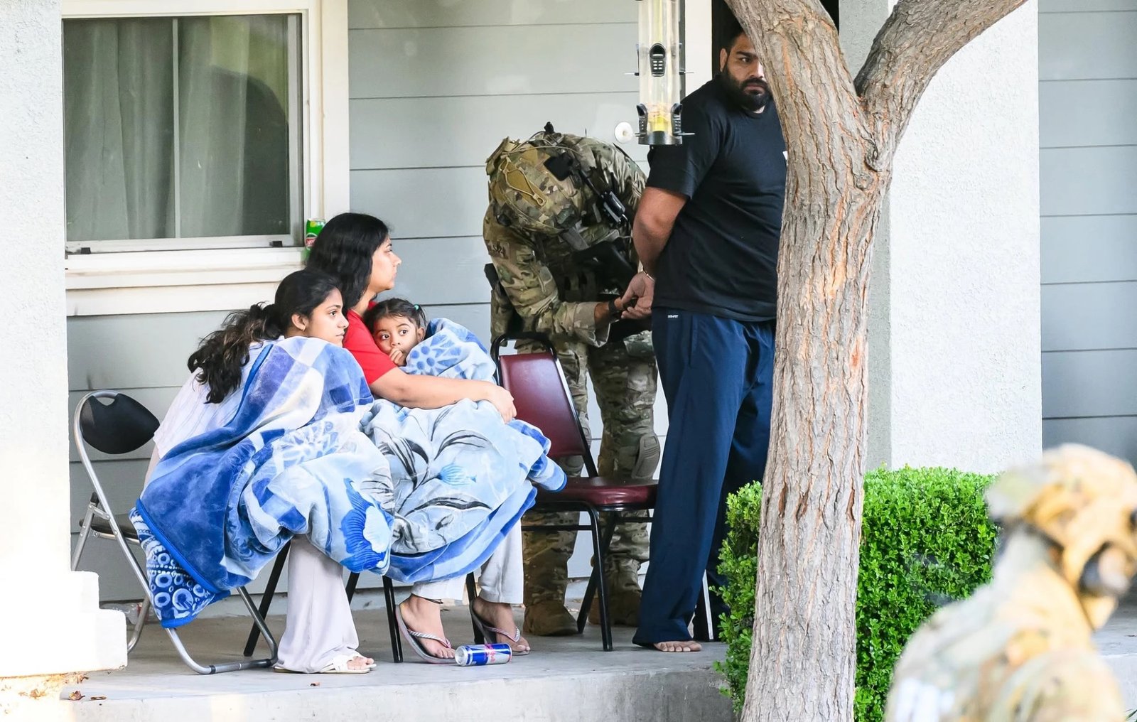 A mother and her children watch as a suspect is handcuffed on the porch.