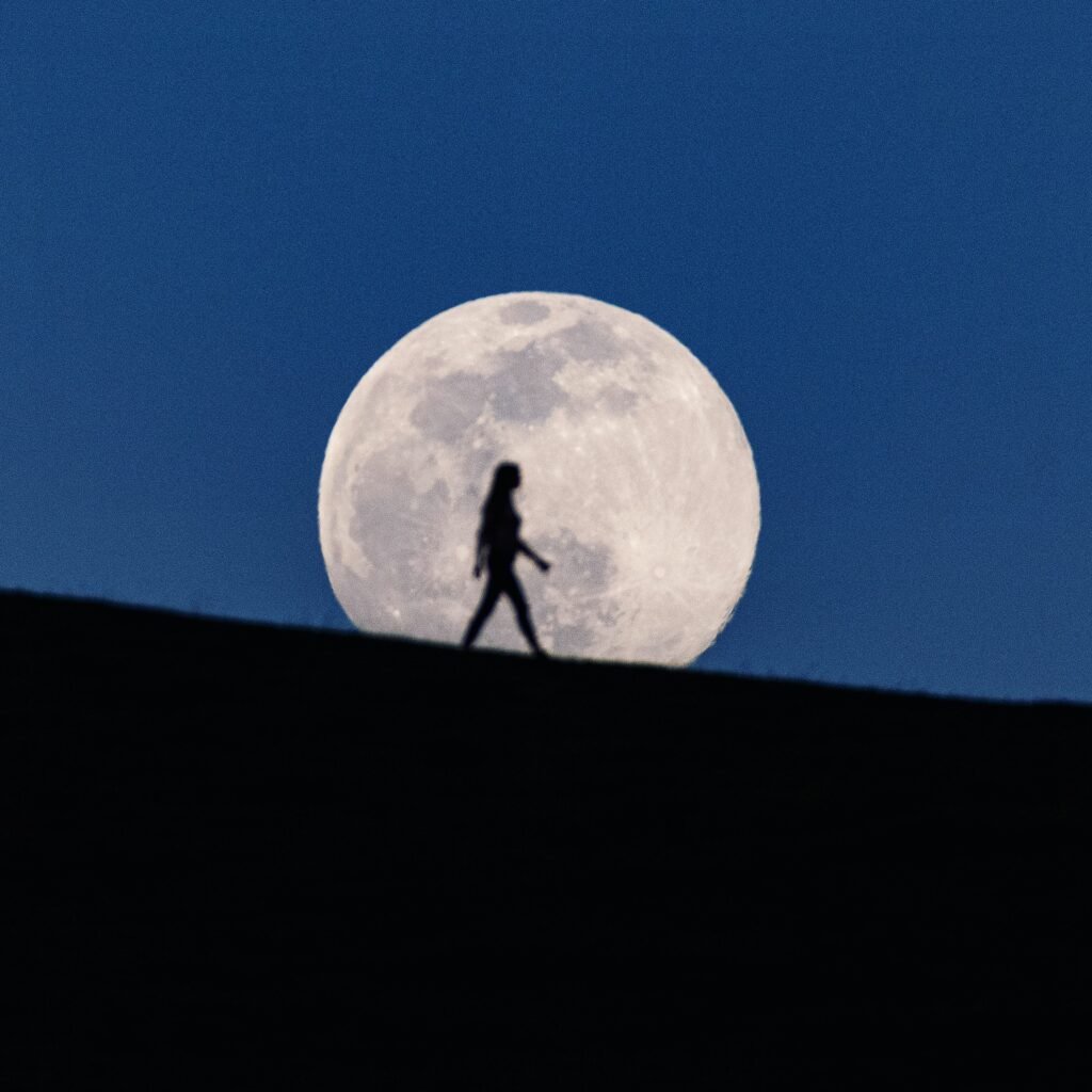 A hiker silhouetted against a giant full moon on a ridgeline, by Josh Edelson
