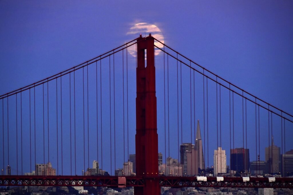 The moon near the Golden Gate Bridge at dusk in San Francisco, by Josh Edelson