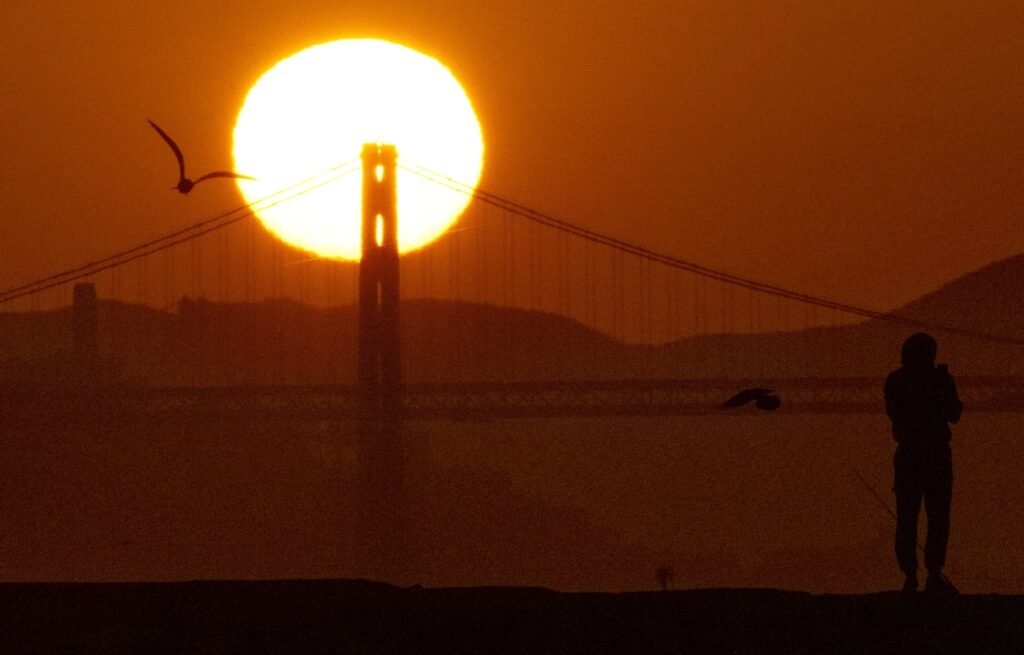 A photographer silhouetted as the sun rises behind the Golden Gate Bridge, by Josh Edelson