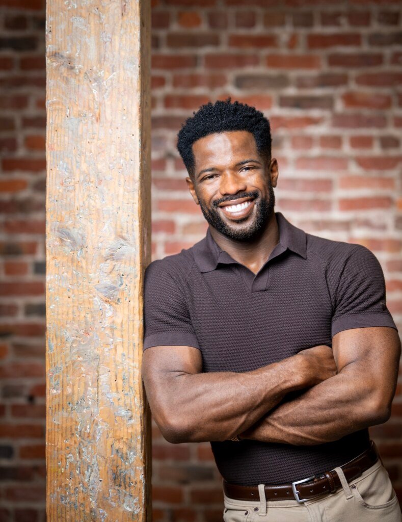 Kevin Caldwell, Ossium Health CEO, arms-crossed portrait at a reclaimed wood beam against brick
