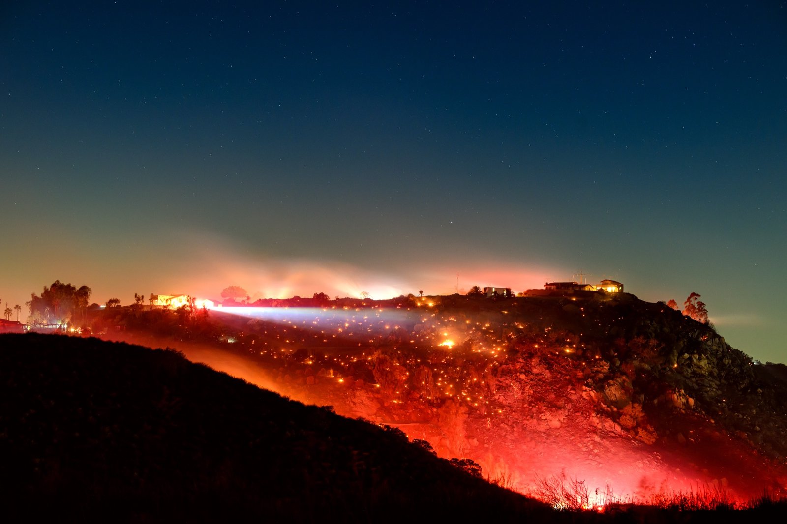 In this long exposure photo, fire smolders on a hillside during the Lilac fire in unincorporated San Diego County, California on January 21, 2025. (Josh Edelson / AFP)