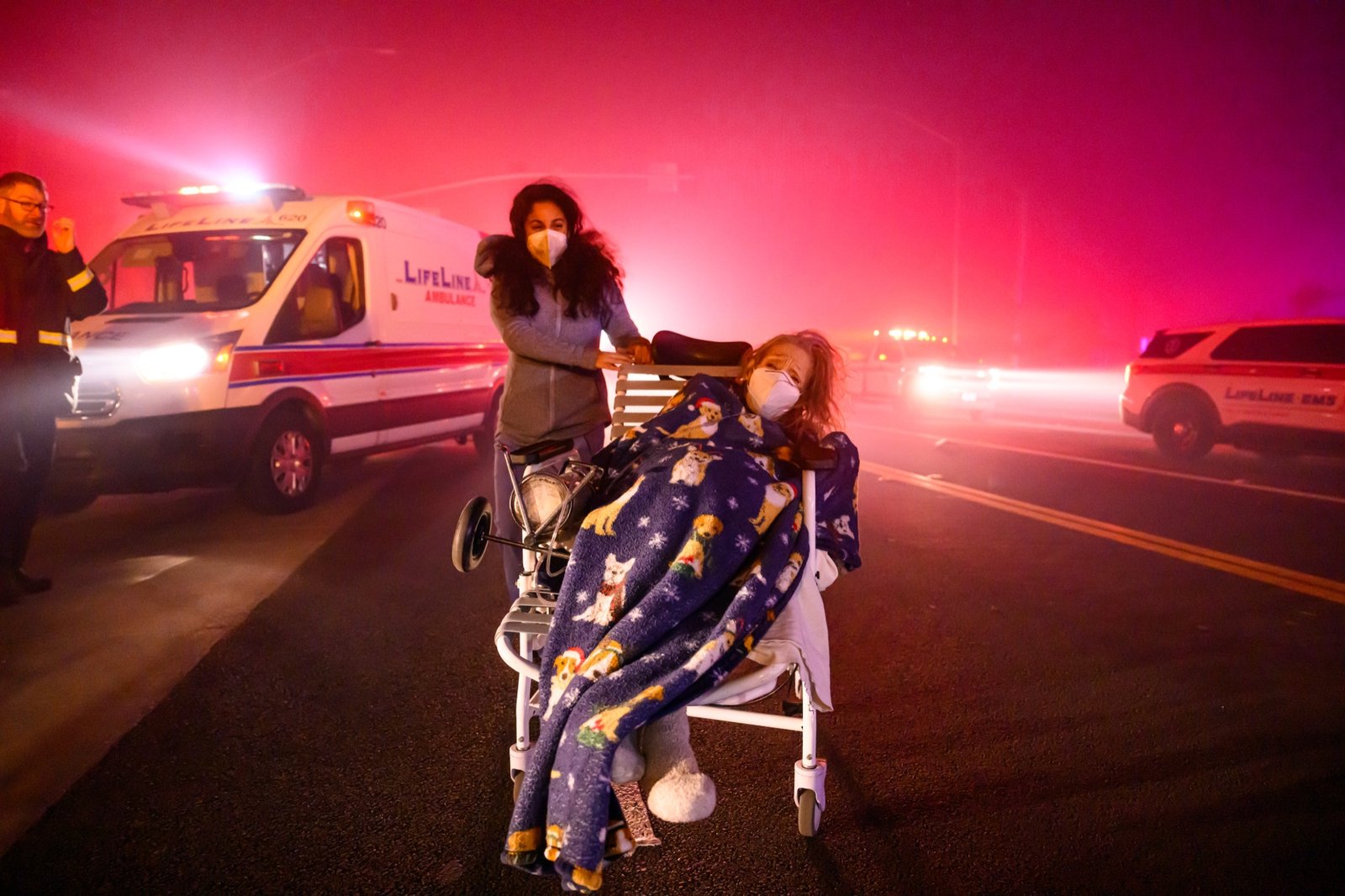 Elderly patients are quickly evacuated into emergency vehicles as embers and flames approach during the Eaton fire in Pasadena, California on January 07, 2025. Multiple fast-moving wildfires broke out in Los Angeles county burning buildings and causing thousands to evacuate as "life threatening" winds whipped the region. Frightened residents abandoned their cars on one of the only roads in and out of the upscale Pacific Palisades area, fleeing on foot from the 770-acre (310-hectare) blaze engulfing an area crammed with multi-million dollar homes in the Santa Monica Mountains. (Josh Edelson / AFP)