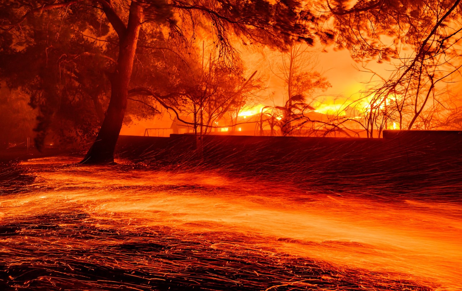 Embers whip across the ground as homes burn during the Eaton fire in Pasadena, California on January 07, 2025. Multiple fast-moving wildfires broke out in Los Angeles county burning buildings and causing thousands to evacuate as "life threatening" winds whipped the region. Frightened residents abandoned their cars on one of the only roads in and out of the upscale Pacific Palisades area, fleeing on foot from the 770-acre (310-hectare) blaze engulfing an area crammed with multi-million dollar homes in the Santa Monica Mountains. (Josh Edelson / AFP)