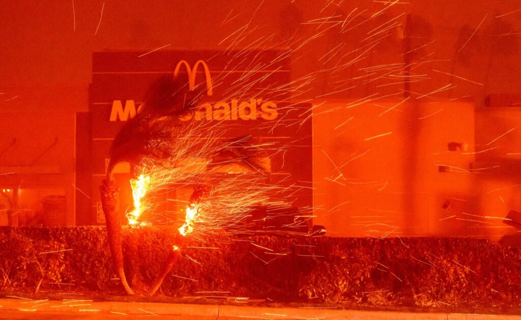 A McDonalds restaurant is showered in embers during the Eaton fire in Pasadena, California on January 07, 2025. Multiple fast-moving wildfires broke out in Los Angeles county burning buildings and causing thousands to evacuate as "life threatening" winds whipped the region. Frightened residents abandoned their cars on one of the only roads in and out of the upscale Pacific Palisades area, fleeing on foot from the 770-acre (310-hectare) blaze engulfing an area crammed with multi-million dollar homes in the Santa Monica Mountains. (Josh Edelson / AFP)