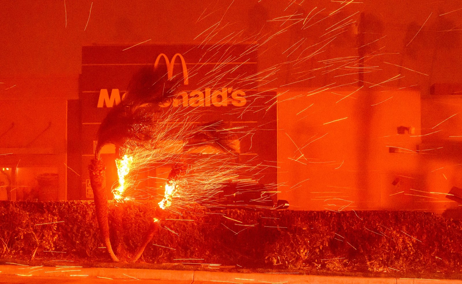 A McDonalds restaurant is showered in embers during the Eaton fire in Pasadena, California on January 07, 2025. Multiple fast-moving wildfires broke out in Los Angeles county burning buildings and causing thousands to evacuate as "life threatening" winds whipped the region. Frightened residents abandoned their cars on one of the only roads in and out of the upscale Pacific Palisades area, fleeing on foot from the 770-acre (310-hectare) blaze engulfing an area crammed with multi-million dollar homes in the Santa Monica Mountains. (Josh Edelson / AFP)