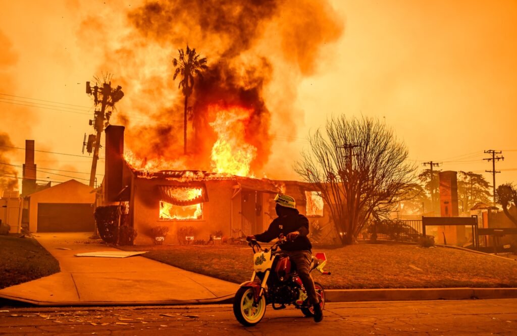A motorcyclist stops to look at a burning home during the Eaton fire in the Altadena area of Los Angeles county, California on January 08, 2025. (Josh Edelson / AFP)