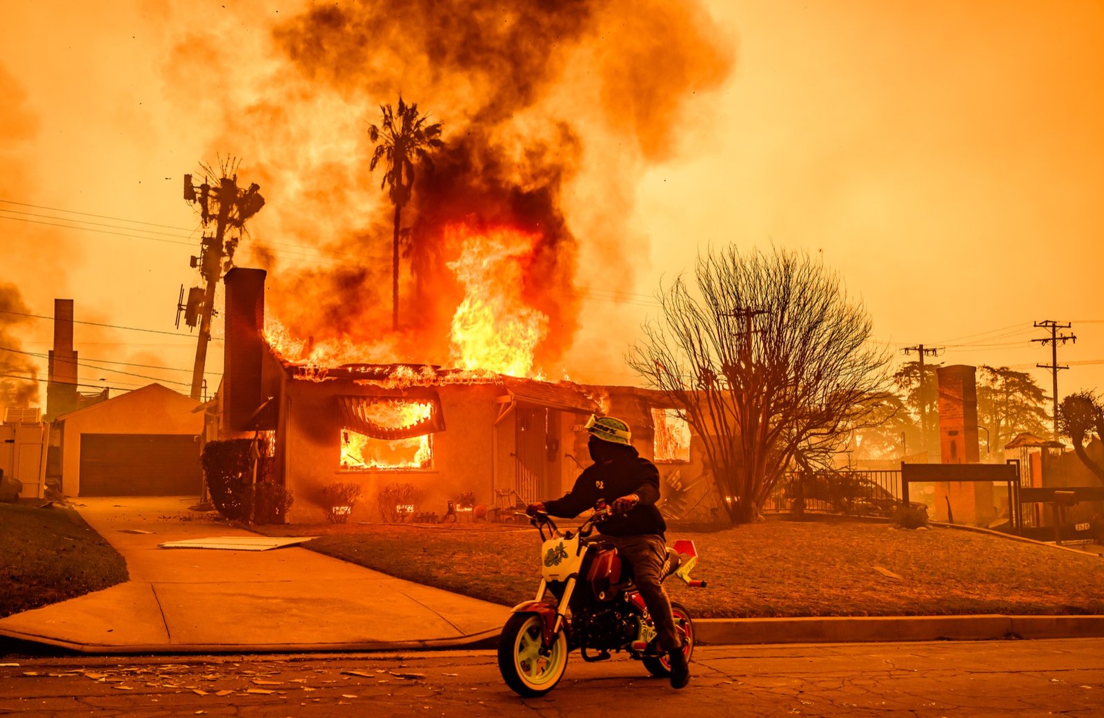 A motorcyclist stops to look at a burning home during the Eaton fire in the Altadena area of Los Angeles county, California on January 08, 2025. (Josh Edelson / AFP)